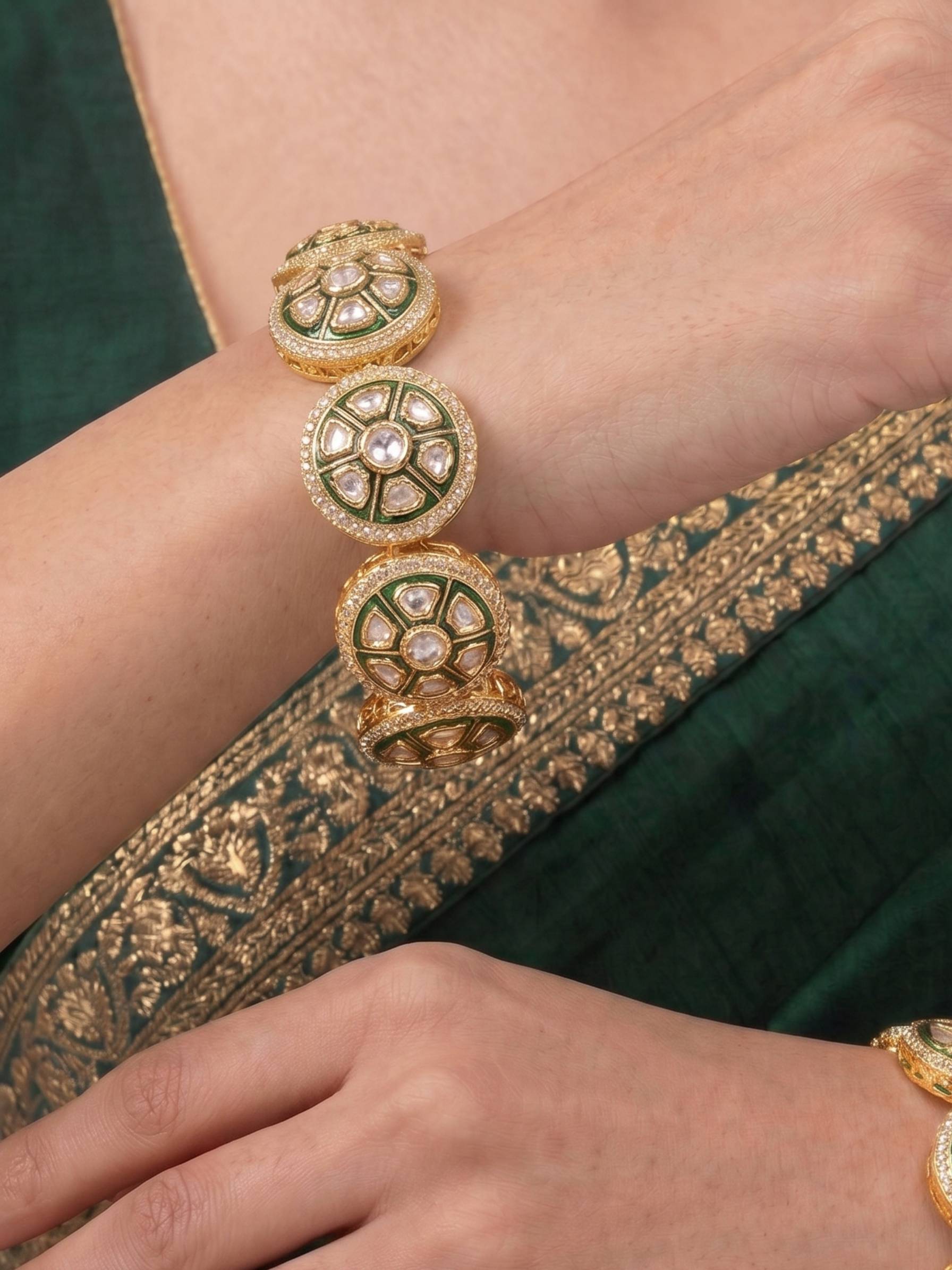 Close-up of a hand wearing a gold bracelet with green accents on a green fabric background.