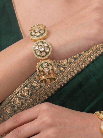 Close-up of a hand wearing a gold bracelet with green accents on a green fabric background.
