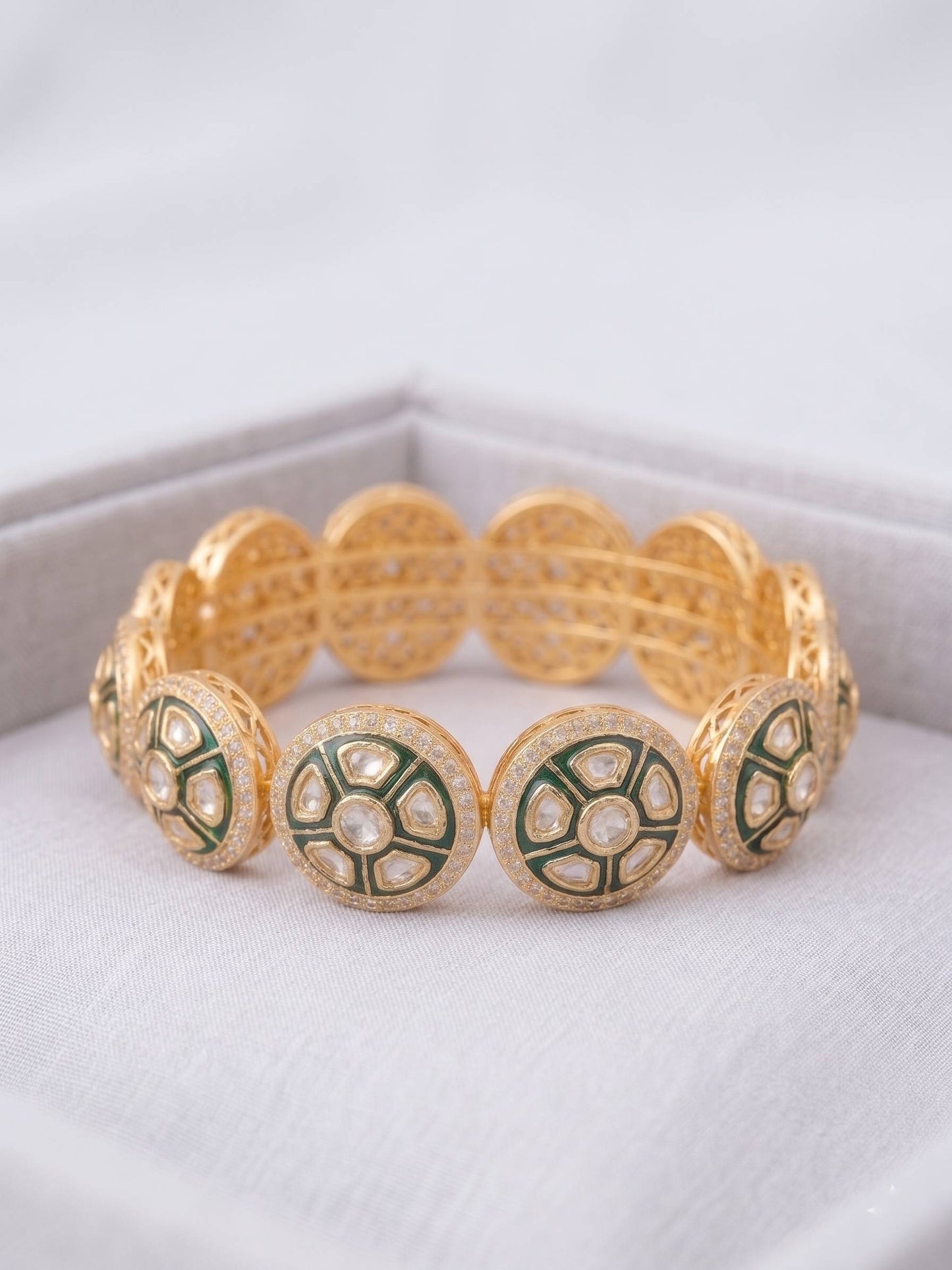 Gold bracelet with green and white circular patterns on a white surface
