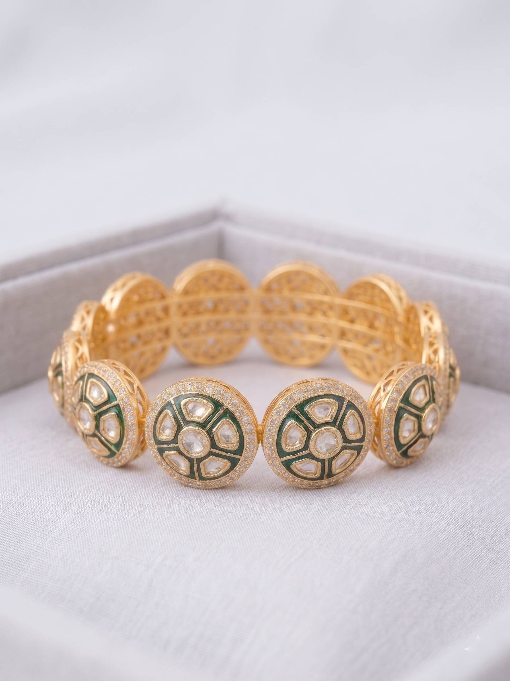 Gold bracelet with green and white circular patterns on a white surface