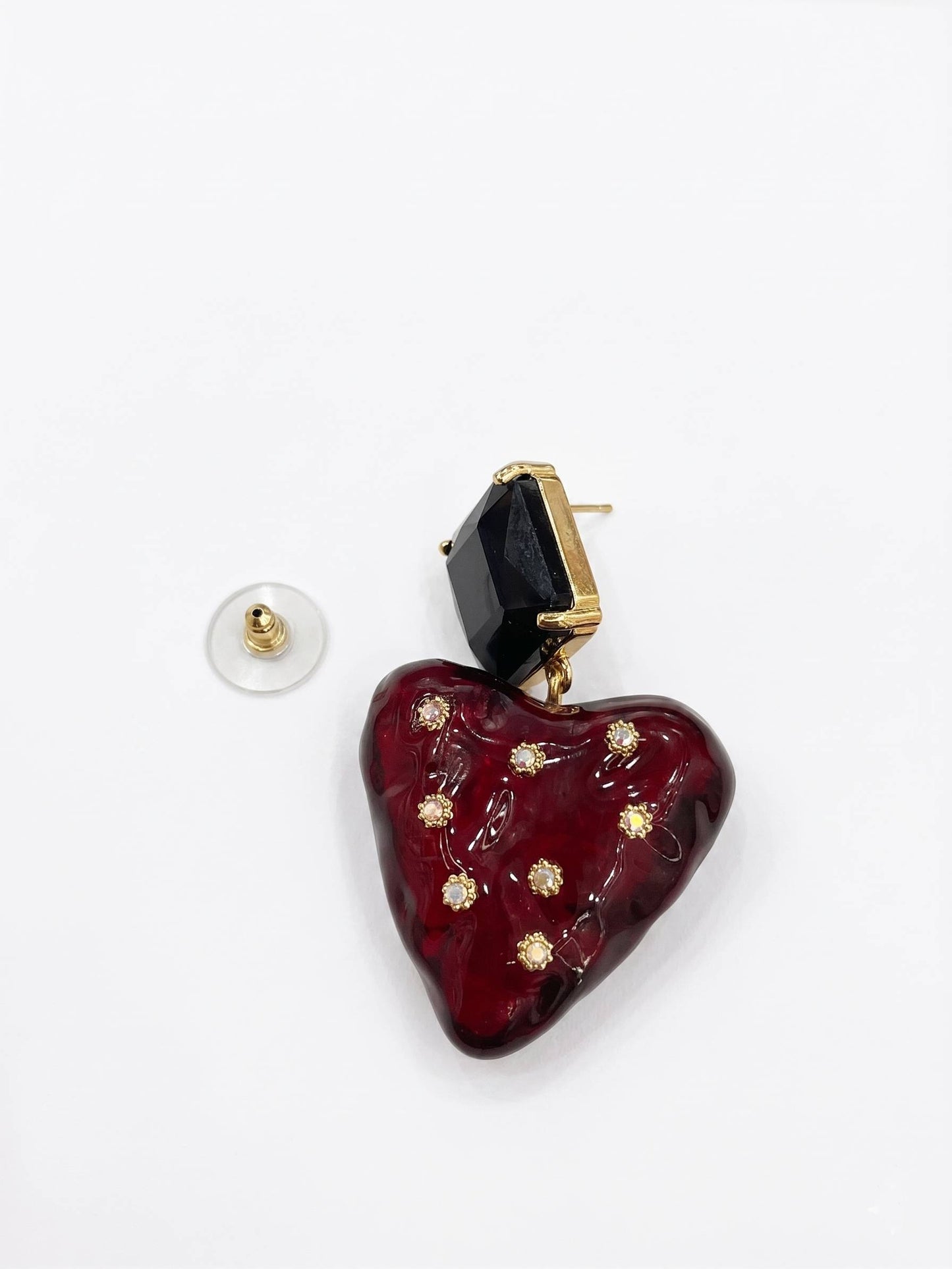 Heart-shaped earring with black gemstone and gold accents on a white background