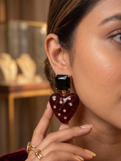 Close-up of a woman wearing a burgundy heart-shaped earring with a black center.