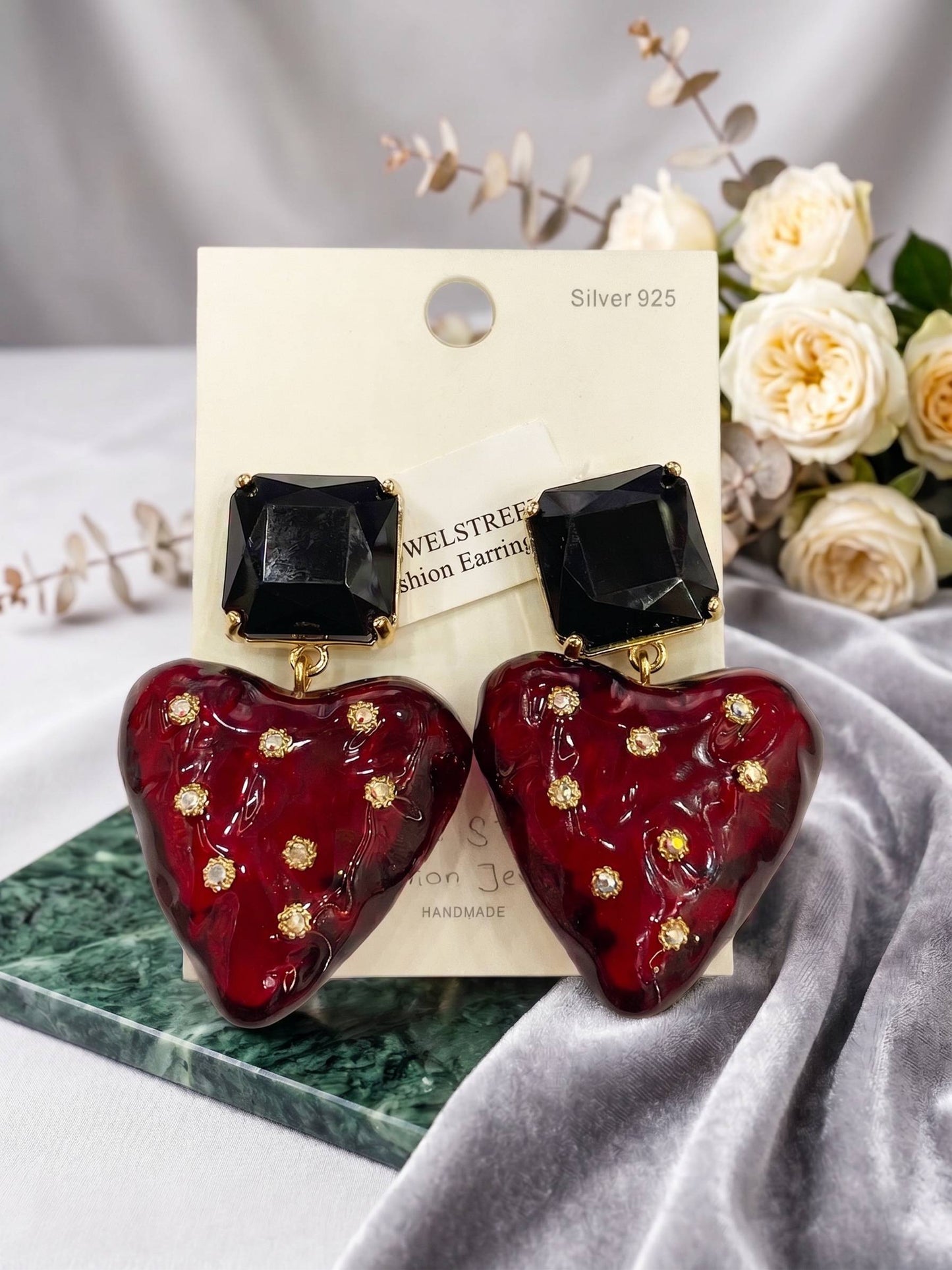 Heart-shaped earrings with black and red design on a card with flowers in the background