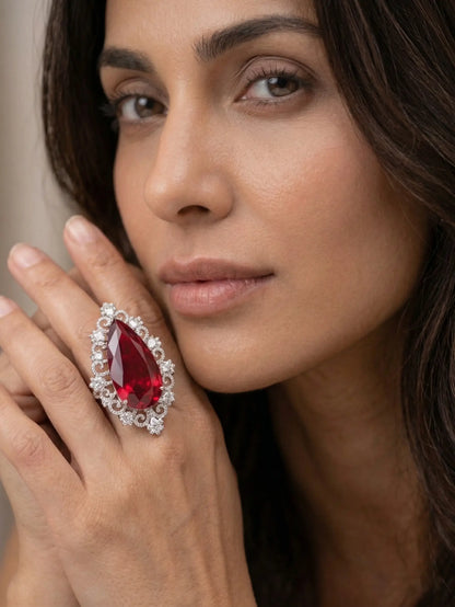 A luxury pear-shaped red cubic zirconia ring with an intricate diamond-style halo on a woman’s finger.
