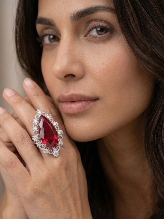 A luxury pear-shaped red cubic zirconia ring with an intricate diamond-style halo on a woman’s finger.