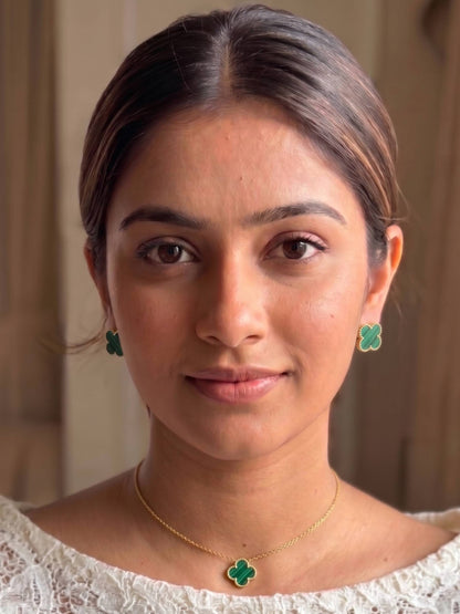 Woman wearing green earrings and a gold necklace with a clover pendant.