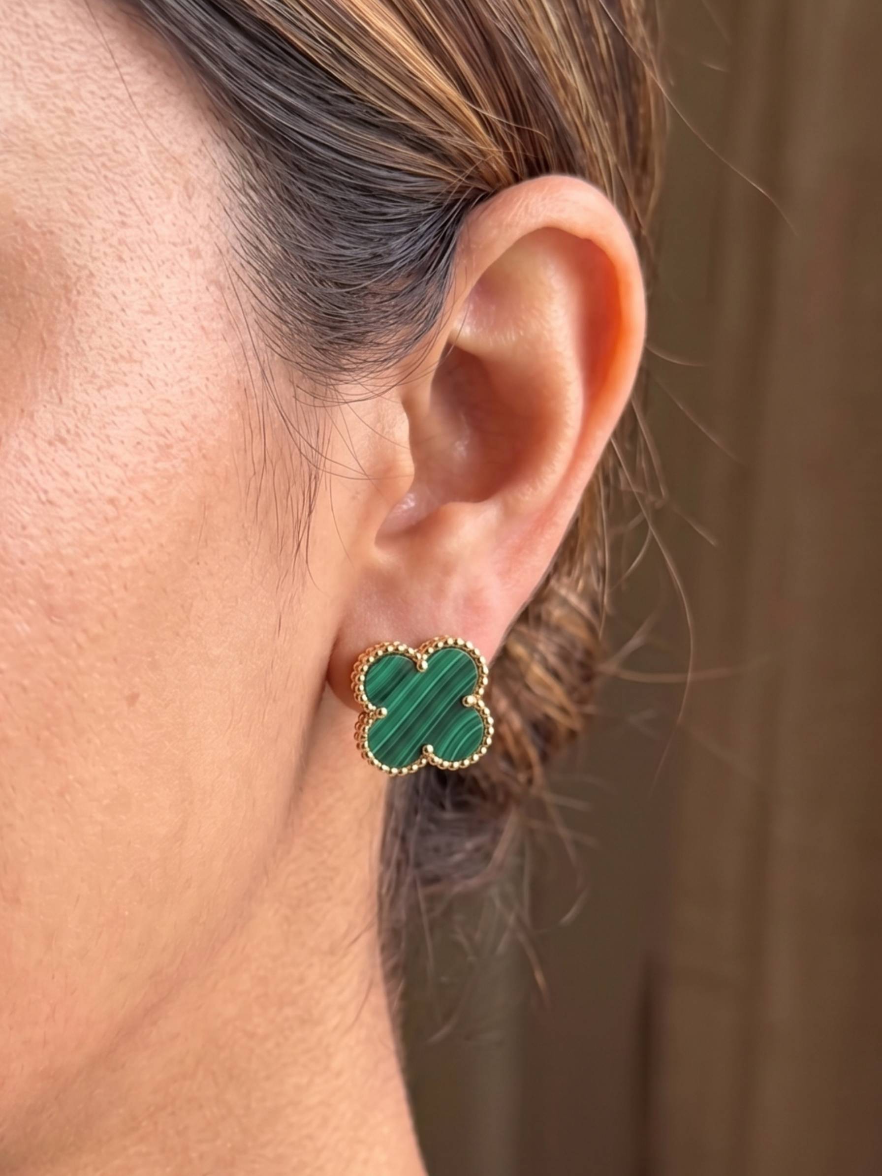 Close-up of an ear wearing a green clover-shaped earring with gold accents.
