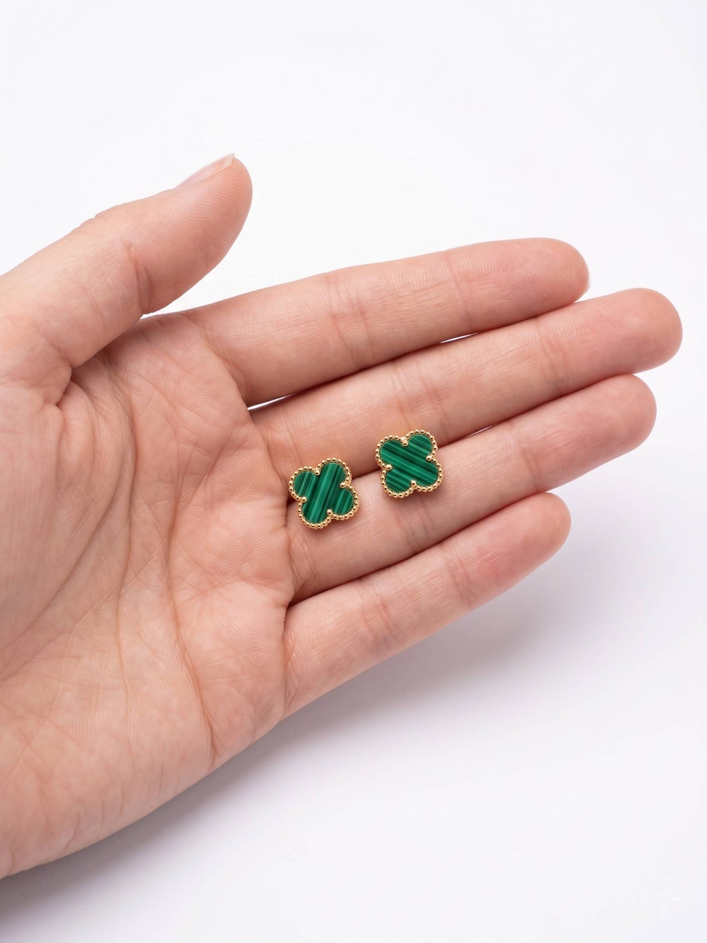 Green clover-shaped earrings held in a hand on a white background