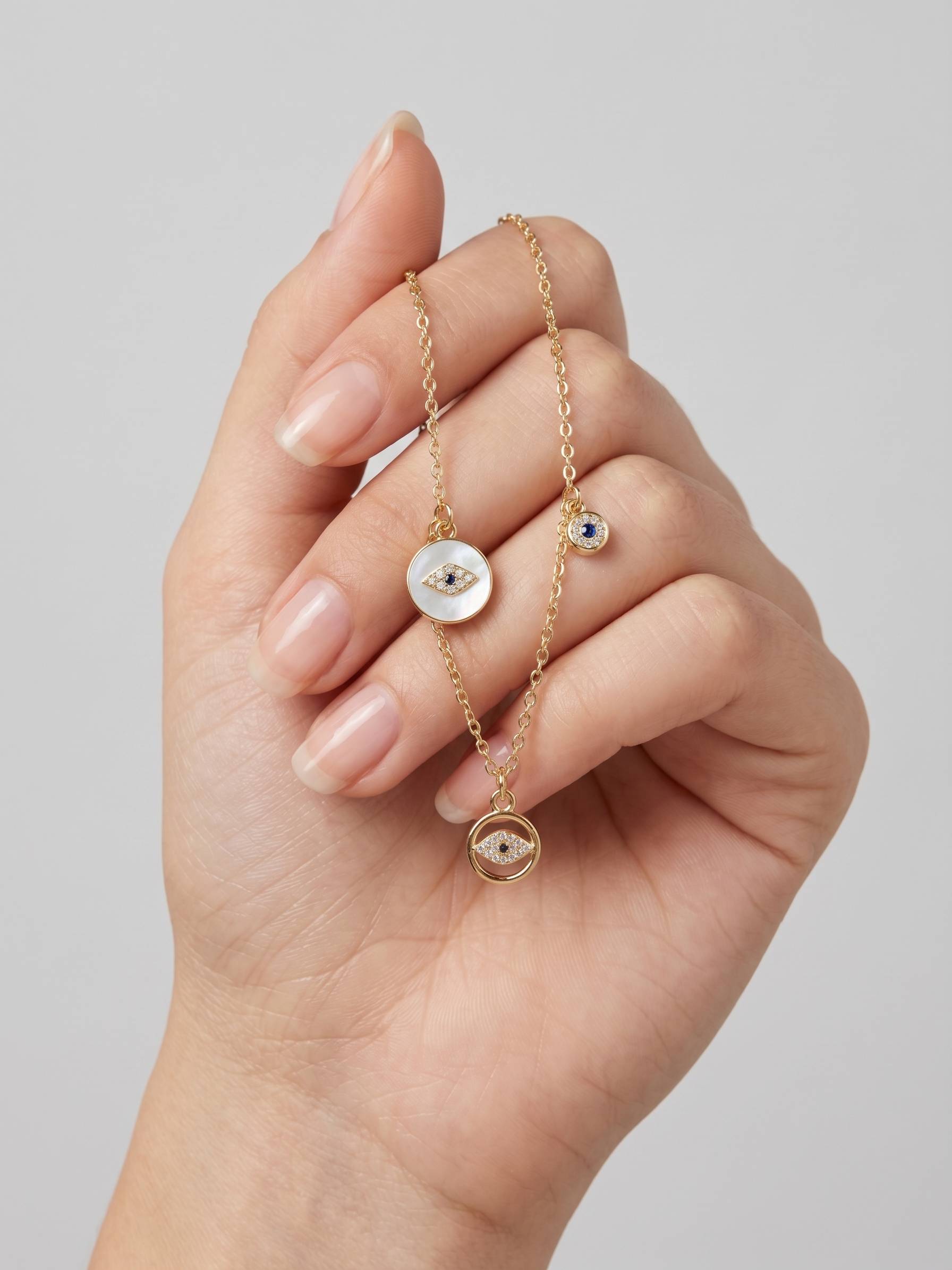 Hand holding a gold necklace with circular pendants against a neutral background