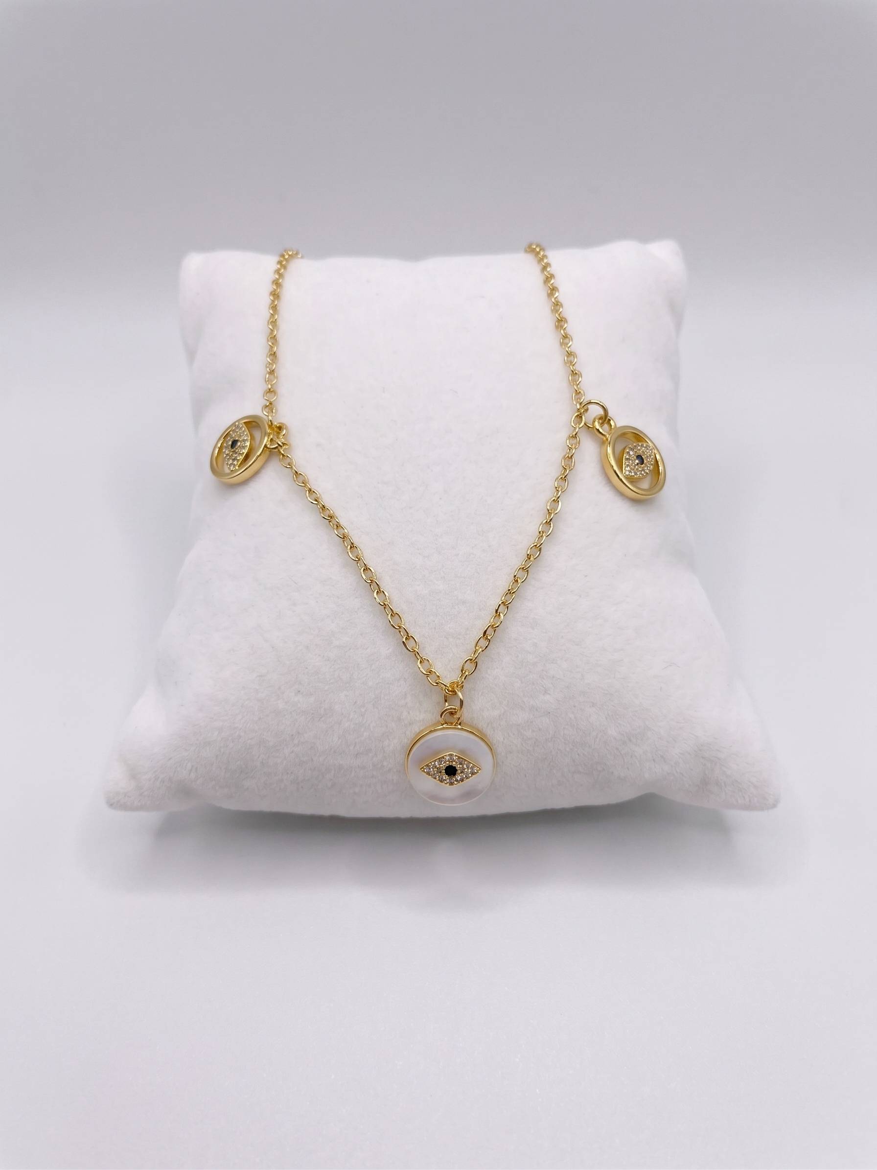 Gold necklace with eye-shaped pendants on a white cushion against a gray background