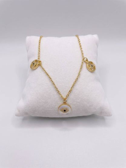 Gold necklace with eye-shaped pendants on a white cushion against a gray background