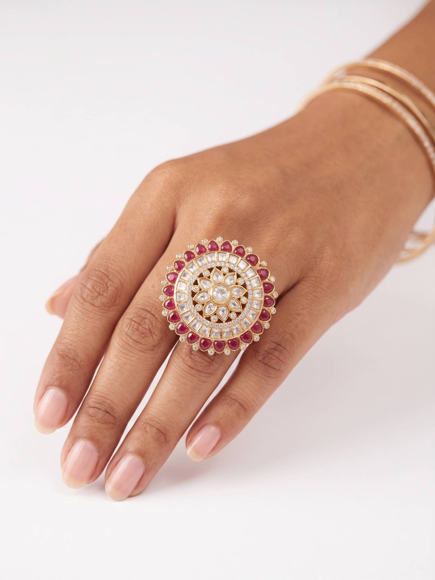 Hand wearing a decorative ring with red stones and pearls on a white background
