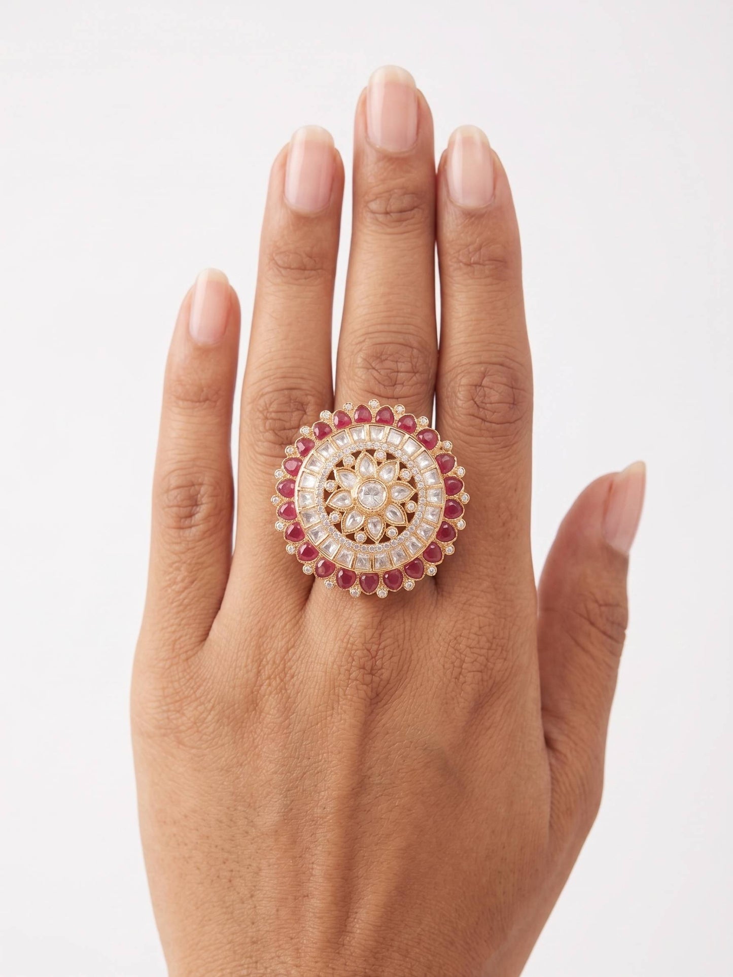 Hand wearing a ring with a circular design and red gemstones on a white background