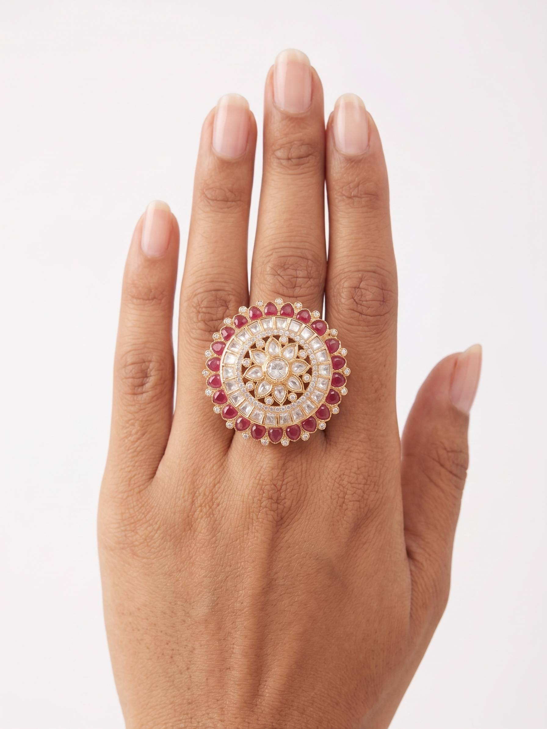 Hand wearing a ring with a circular design and red gemstones on a white background