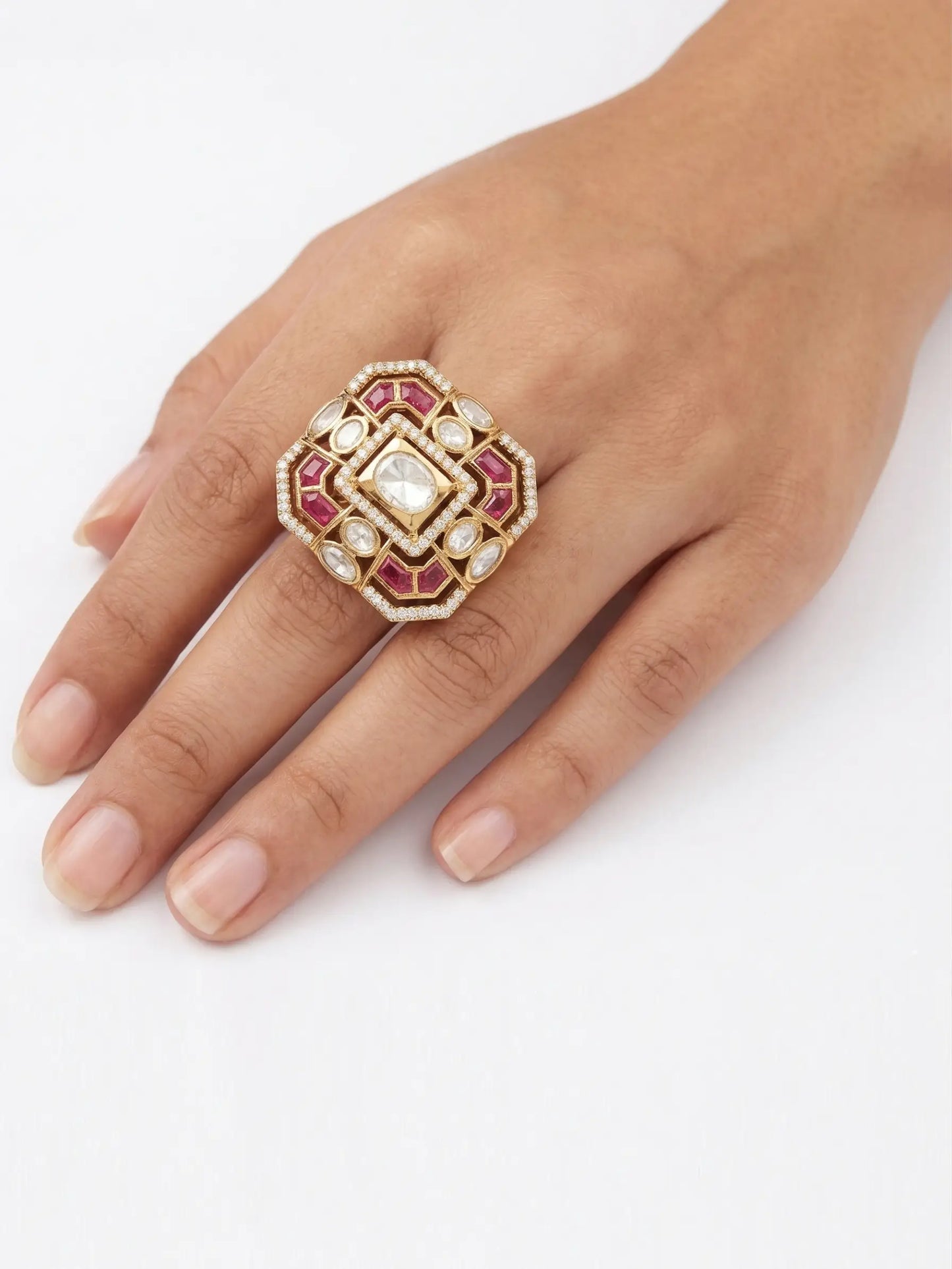 Decorative ring with red stones and gold accents on a hand against a white background