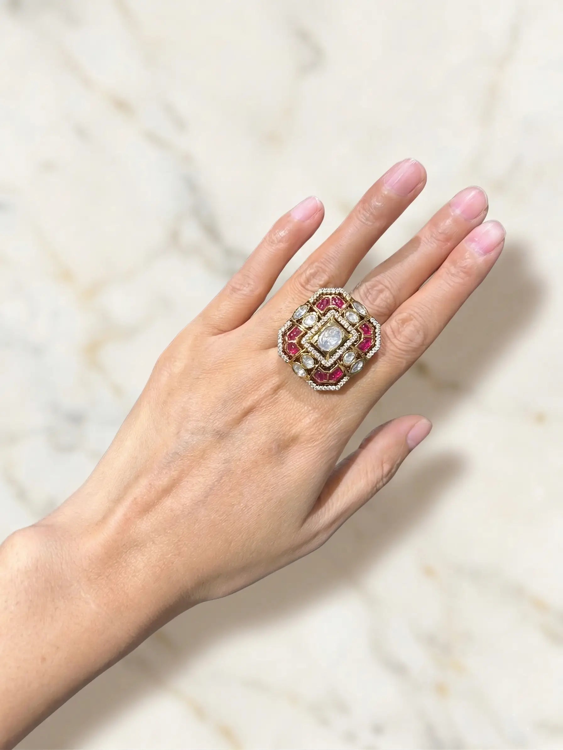Hand wearing a decorative ring with gemstones on a light background