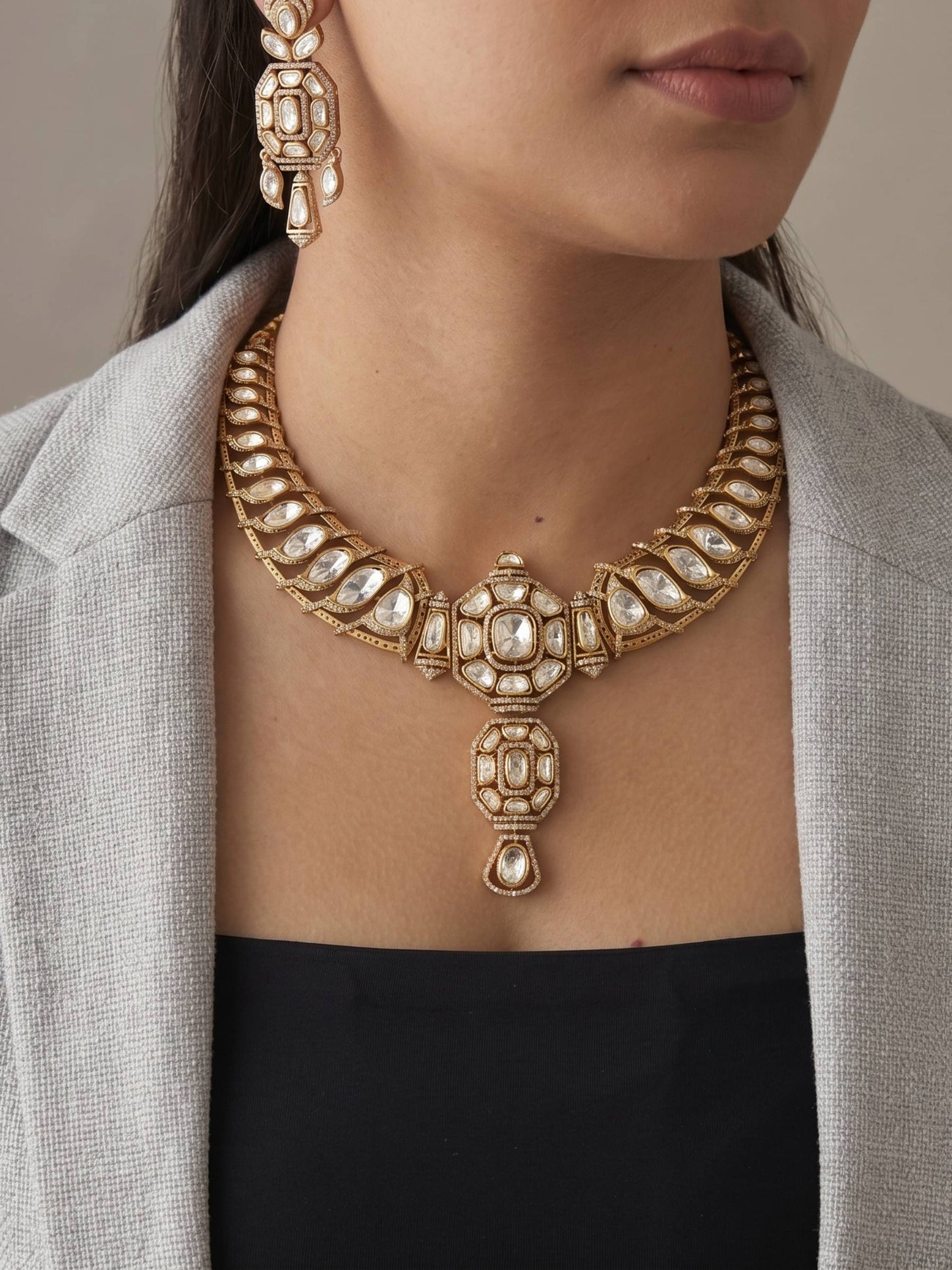 Close-up of a person wearing an ornate gold necklace and earrings against a neutral background