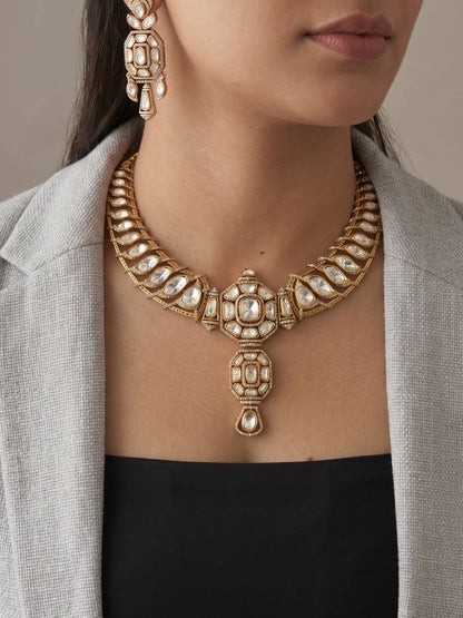 Close-up of a person wearing an ornate gold necklace and earrings against a neutral background