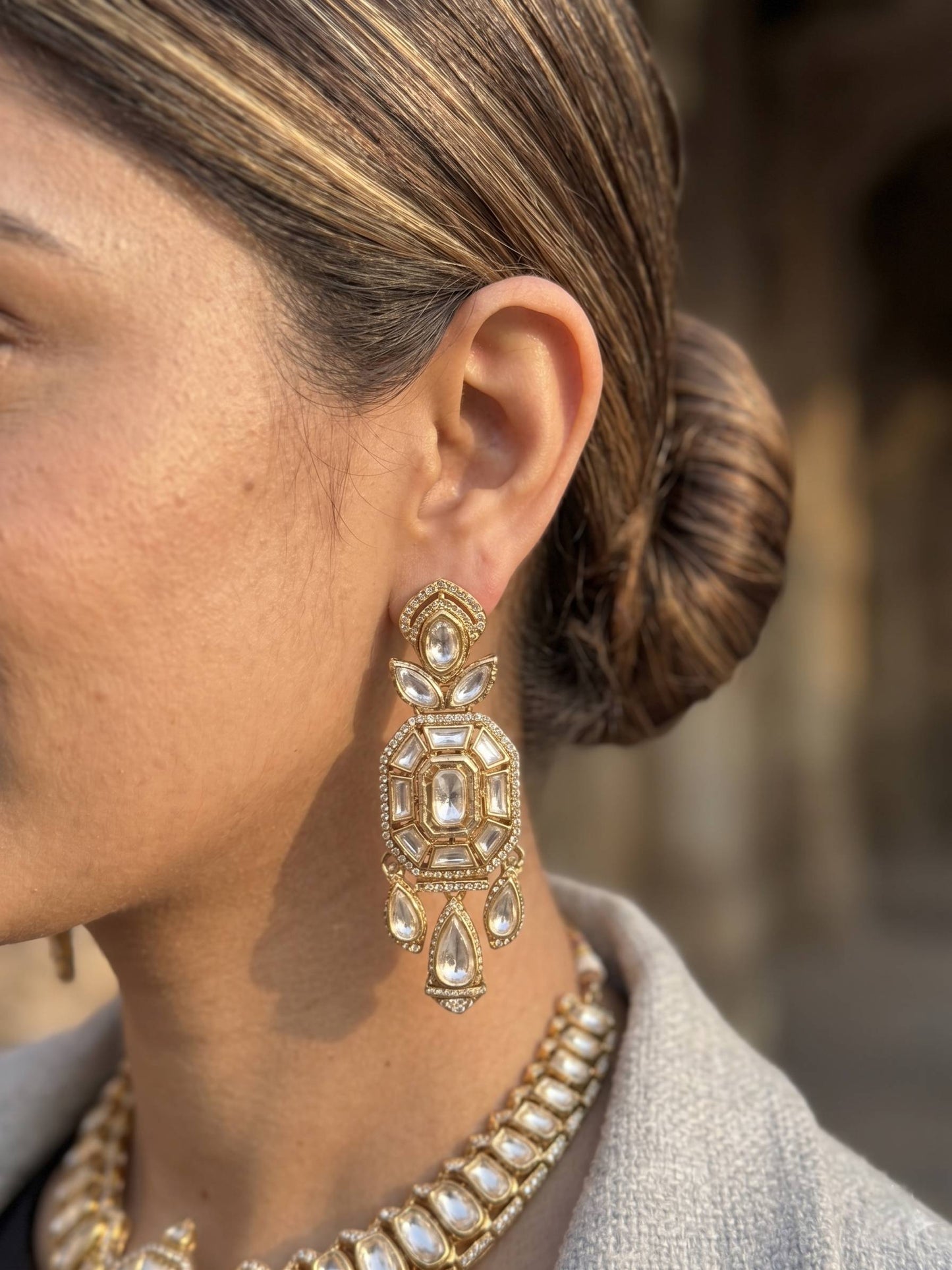 Close-up of a person wearing gold earrings and a necklace with a blurred background