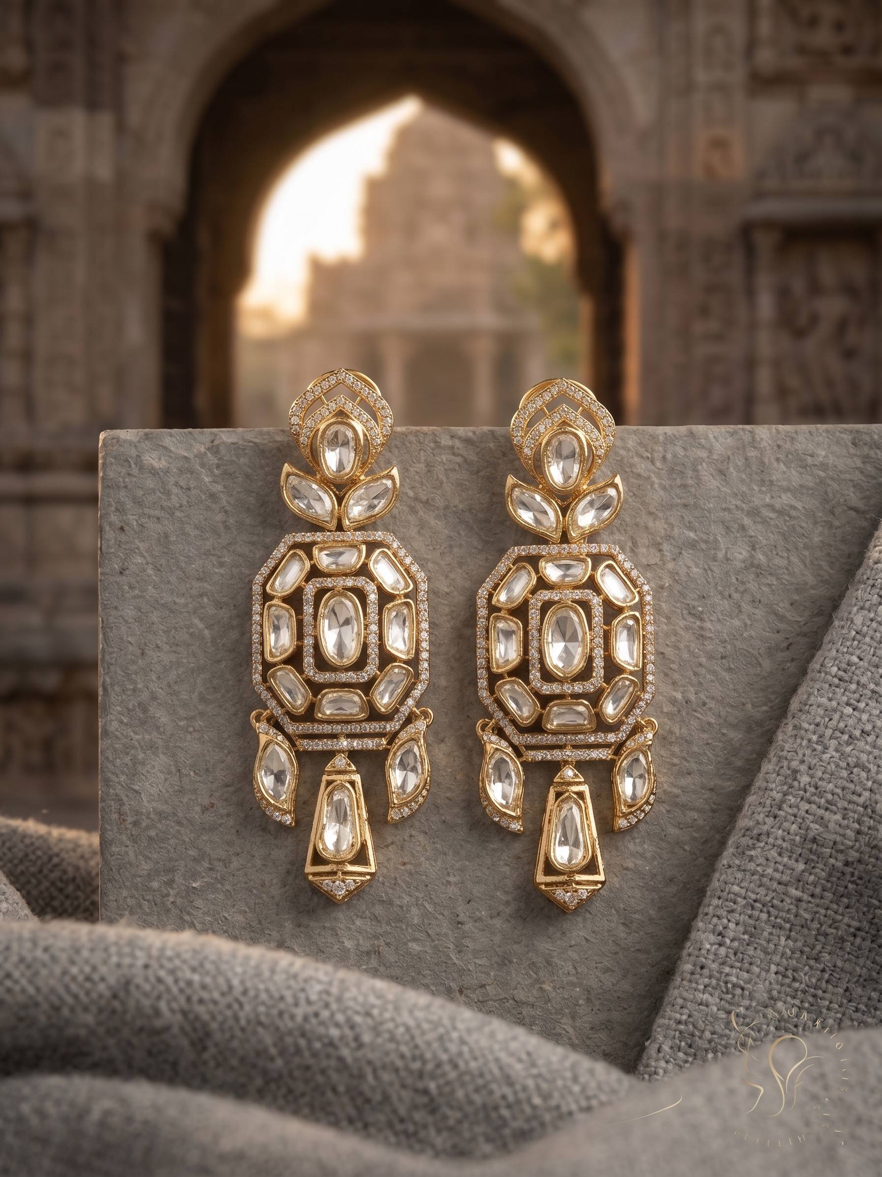 Ornate gold earrings with gemstones on a textured surface with architectural background