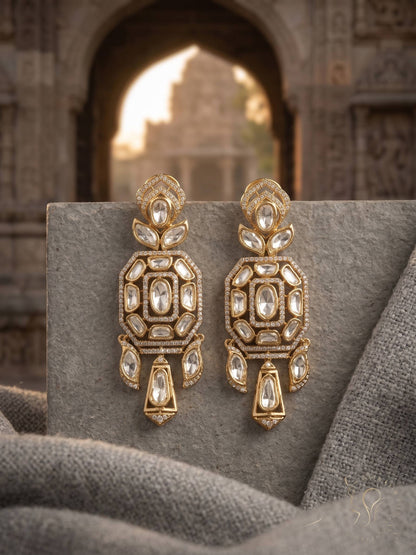 Ornate gold earrings with gemstones on a textured surface with architectural background