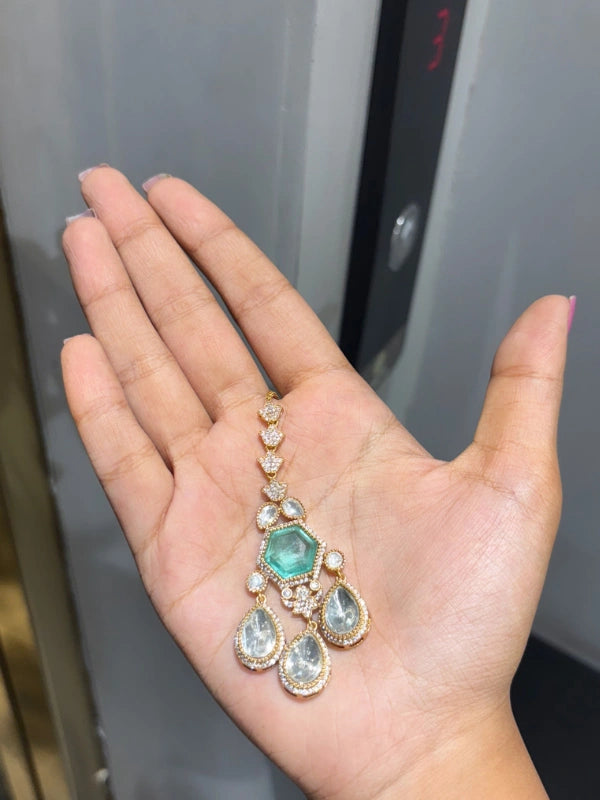 Hand holding a decorative necklace with green gemstone against a neutral background