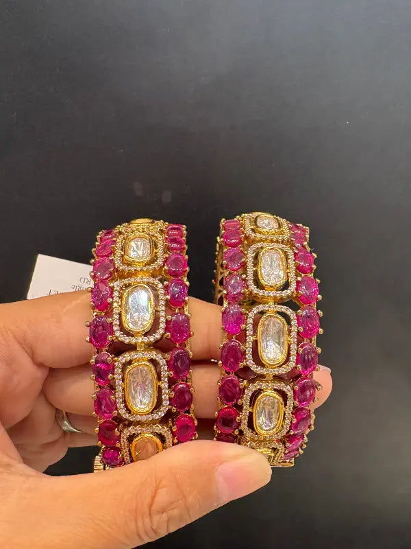 Gold and red gemstone earrings held by a hand against a dark background
