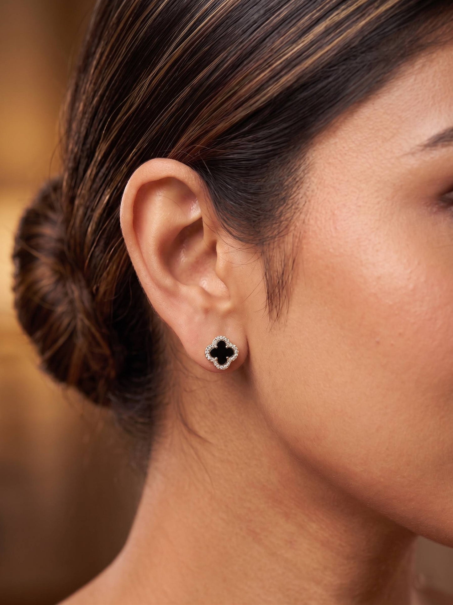 Close-up of a woman's ear wearing a clover-shaped earring with a blurred background