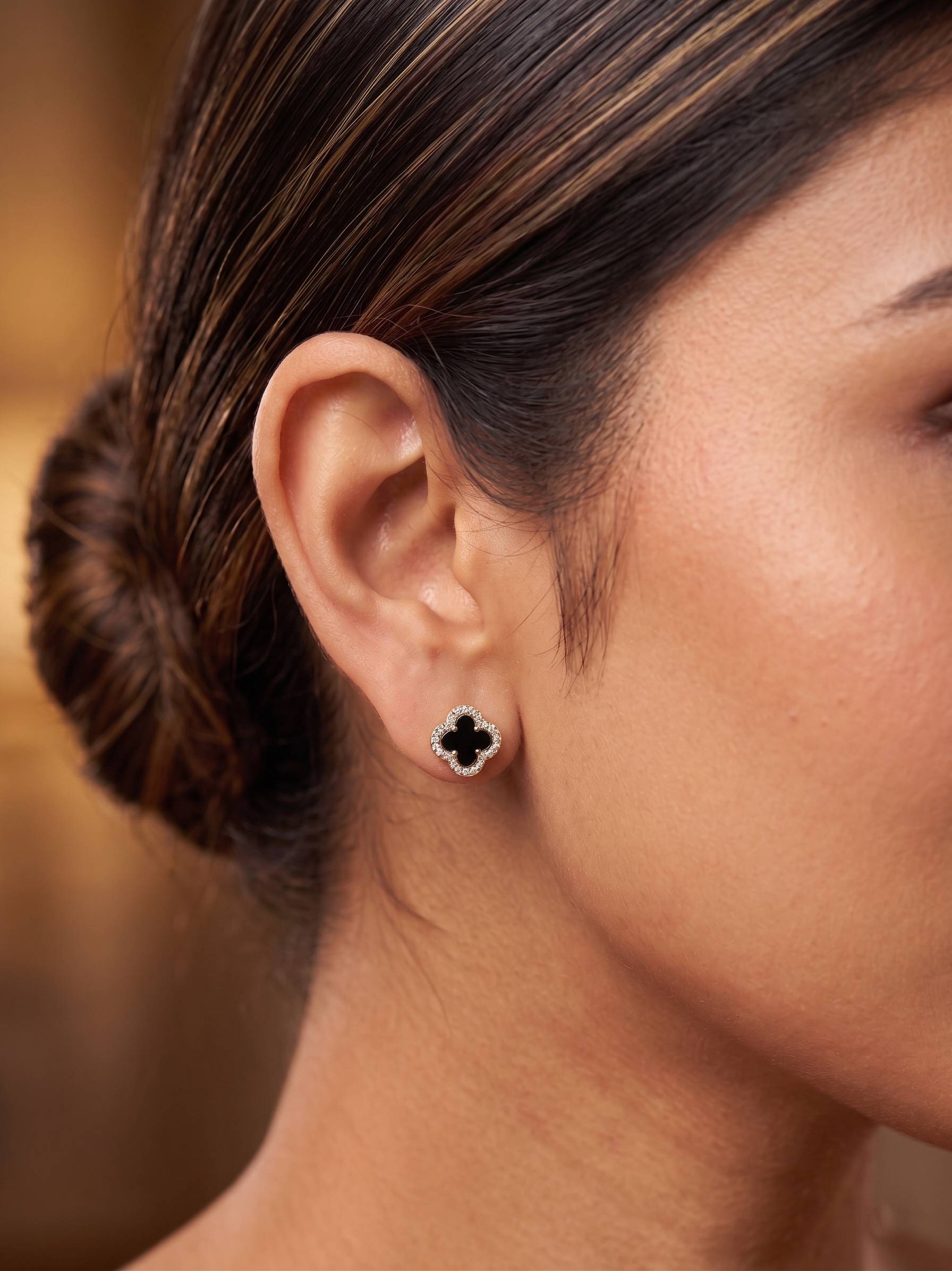 Close-up of a woman's ear wearing a clover-shaped earring with a blurred background