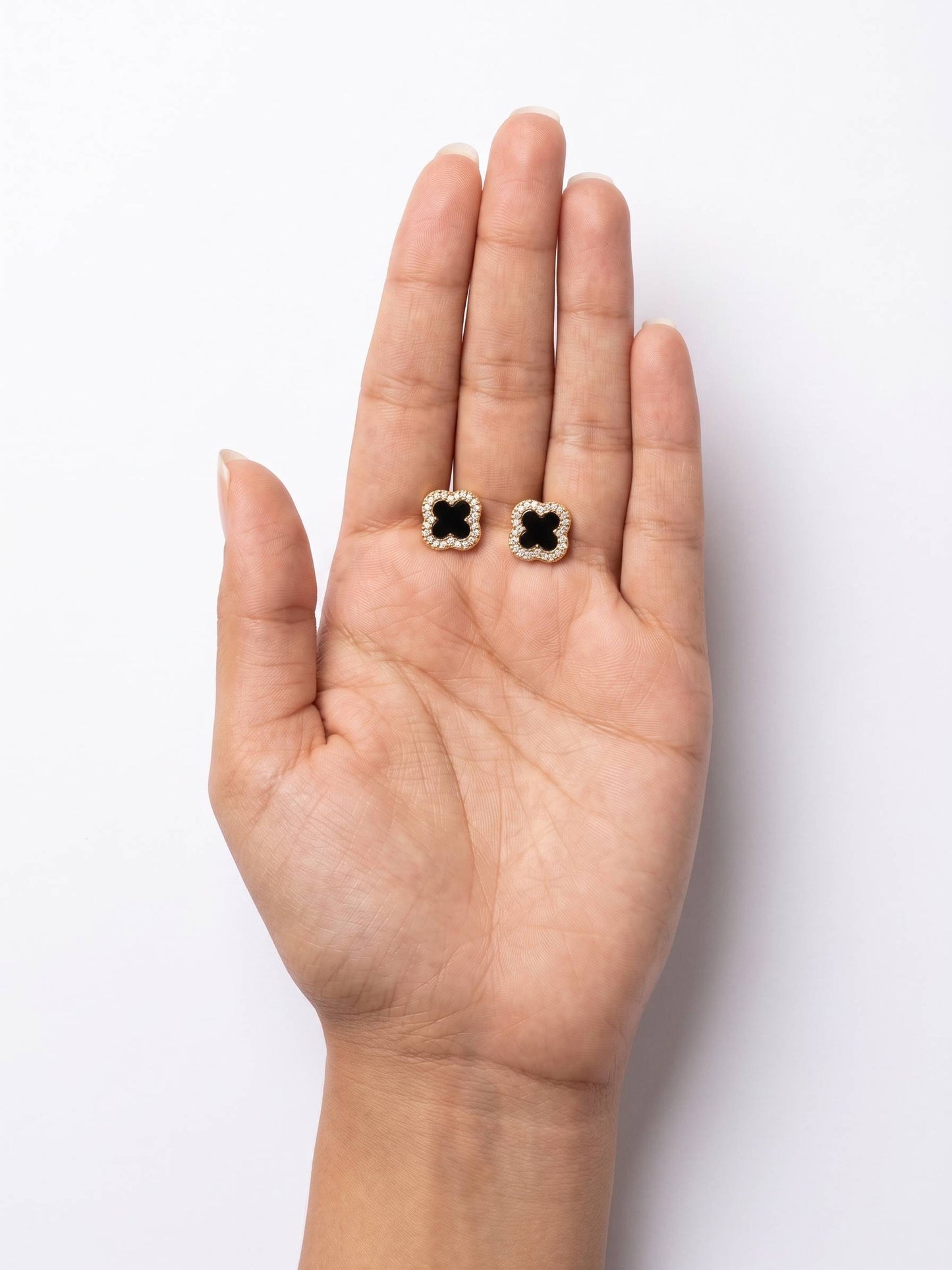 Black and white floral earrings held in a hand on a white background