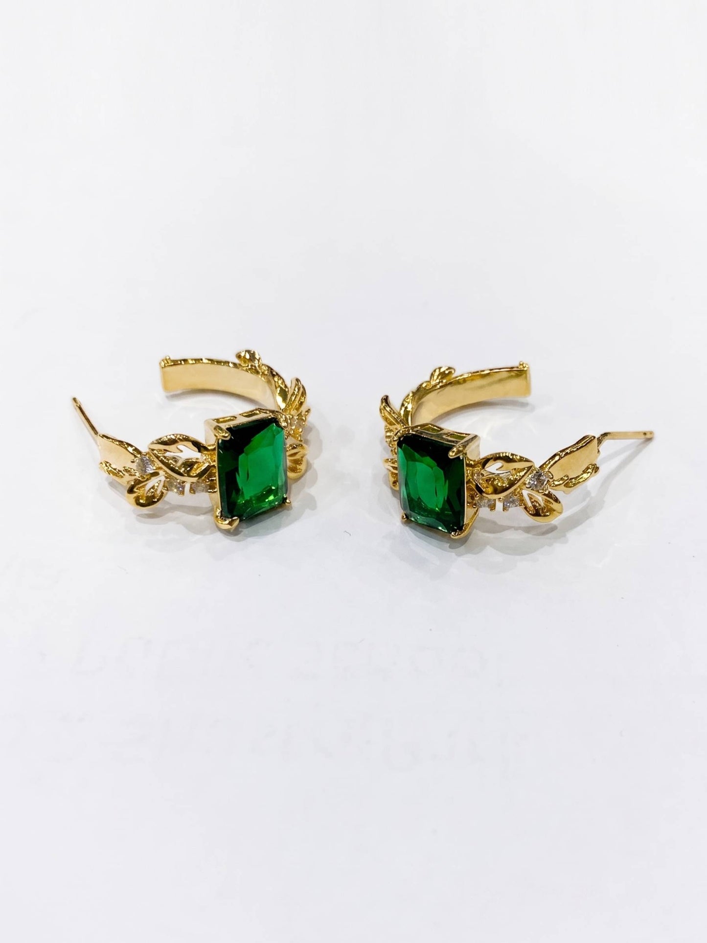 Gold earrings with green gemstones on a white background