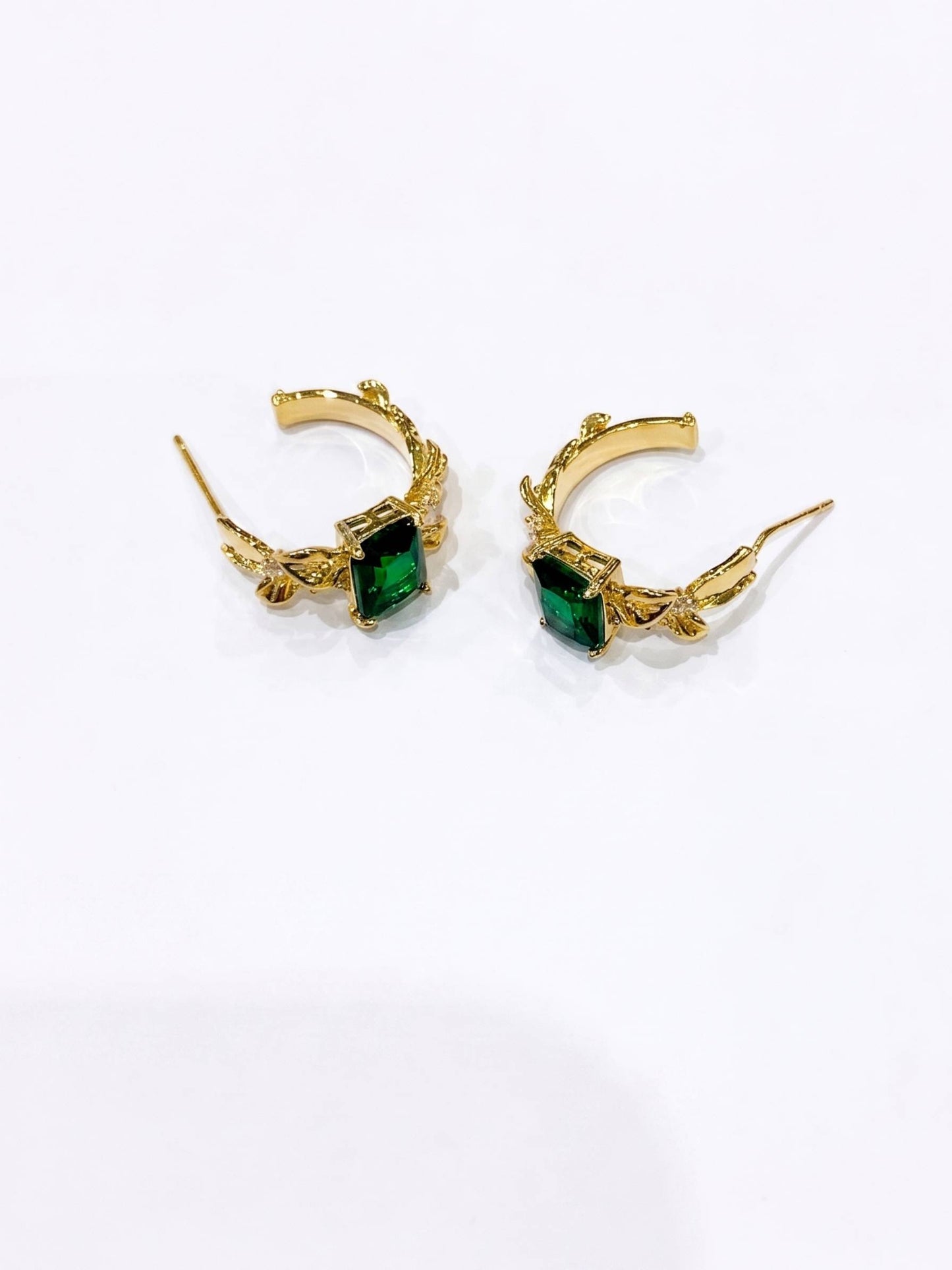 Gold hoop earrings with green gemstones on a white background