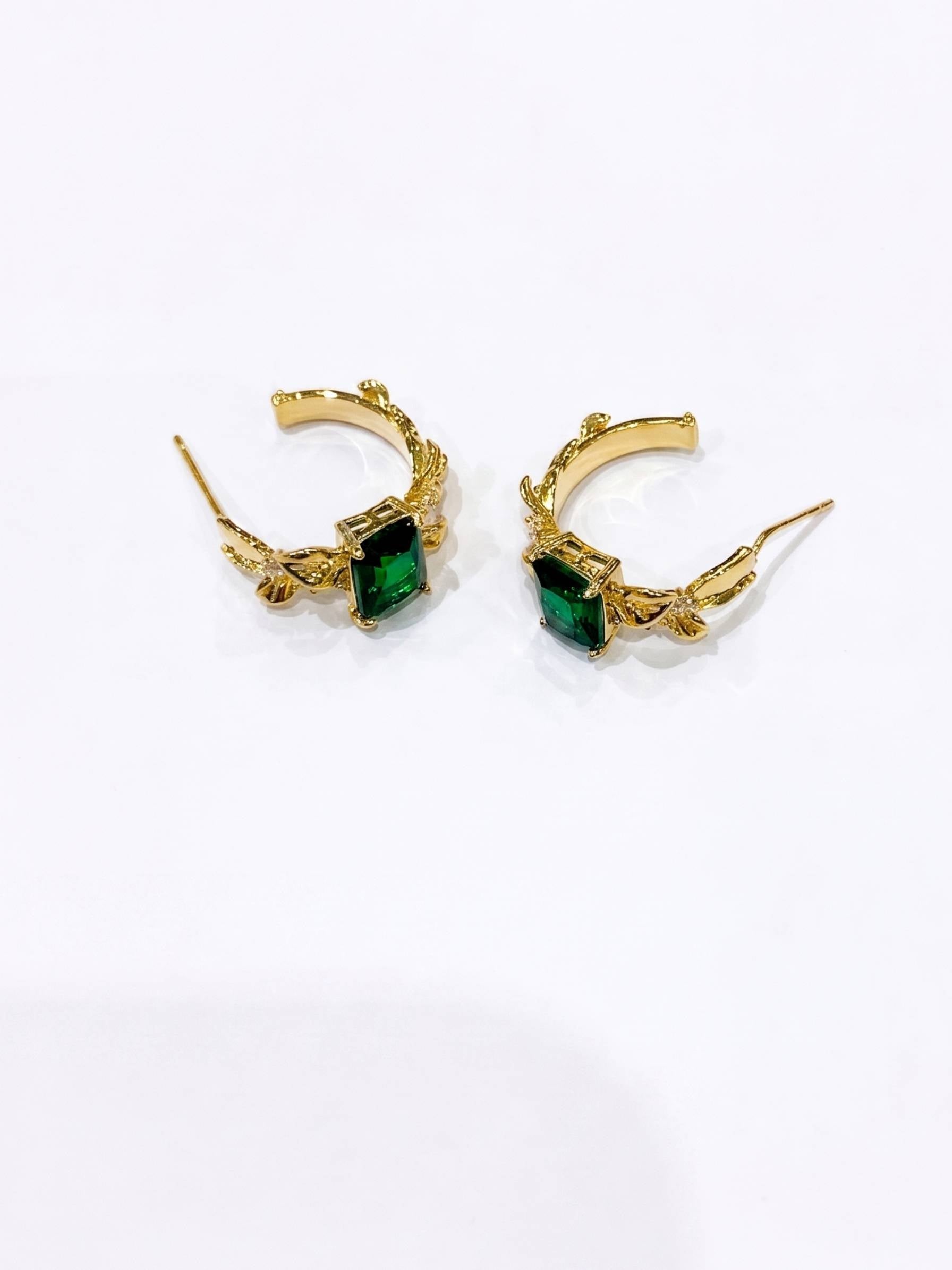 Gold hoop earrings with green gemstones on a white background
