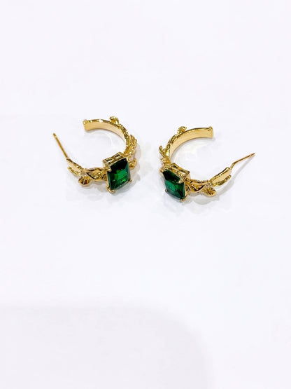 Gold hoop earrings with green gemstones on a white background