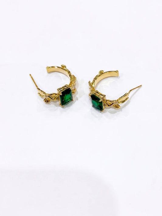 Gold hoop earrings with green gemstones on a white background