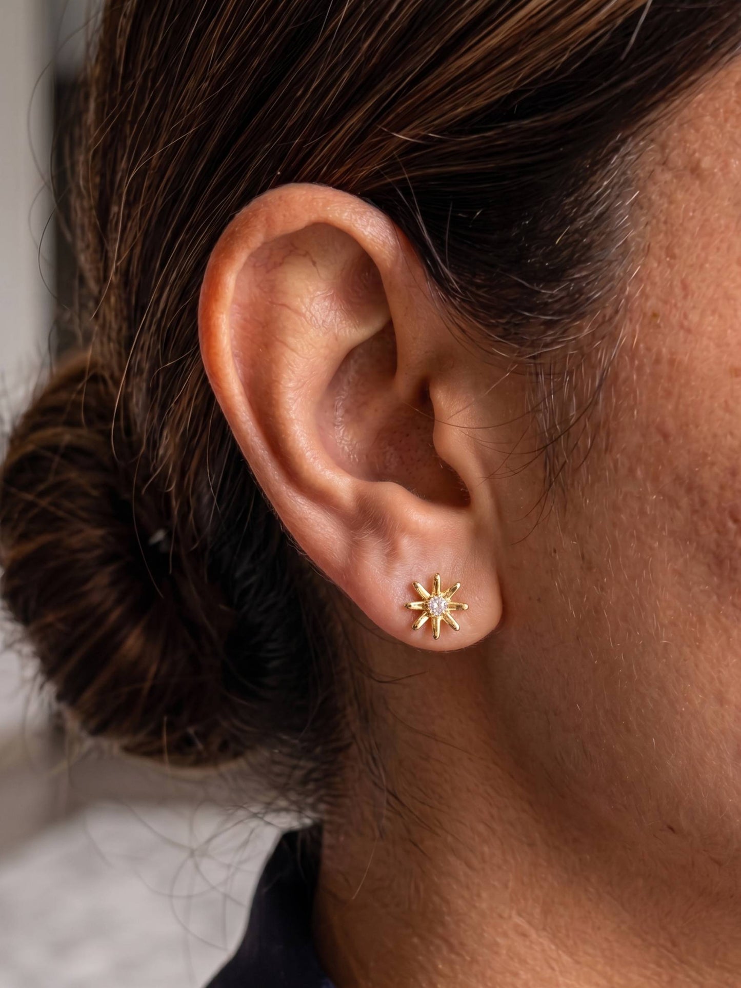 Close-up of an ear wearing a gold star-shaped earring with a blurred background