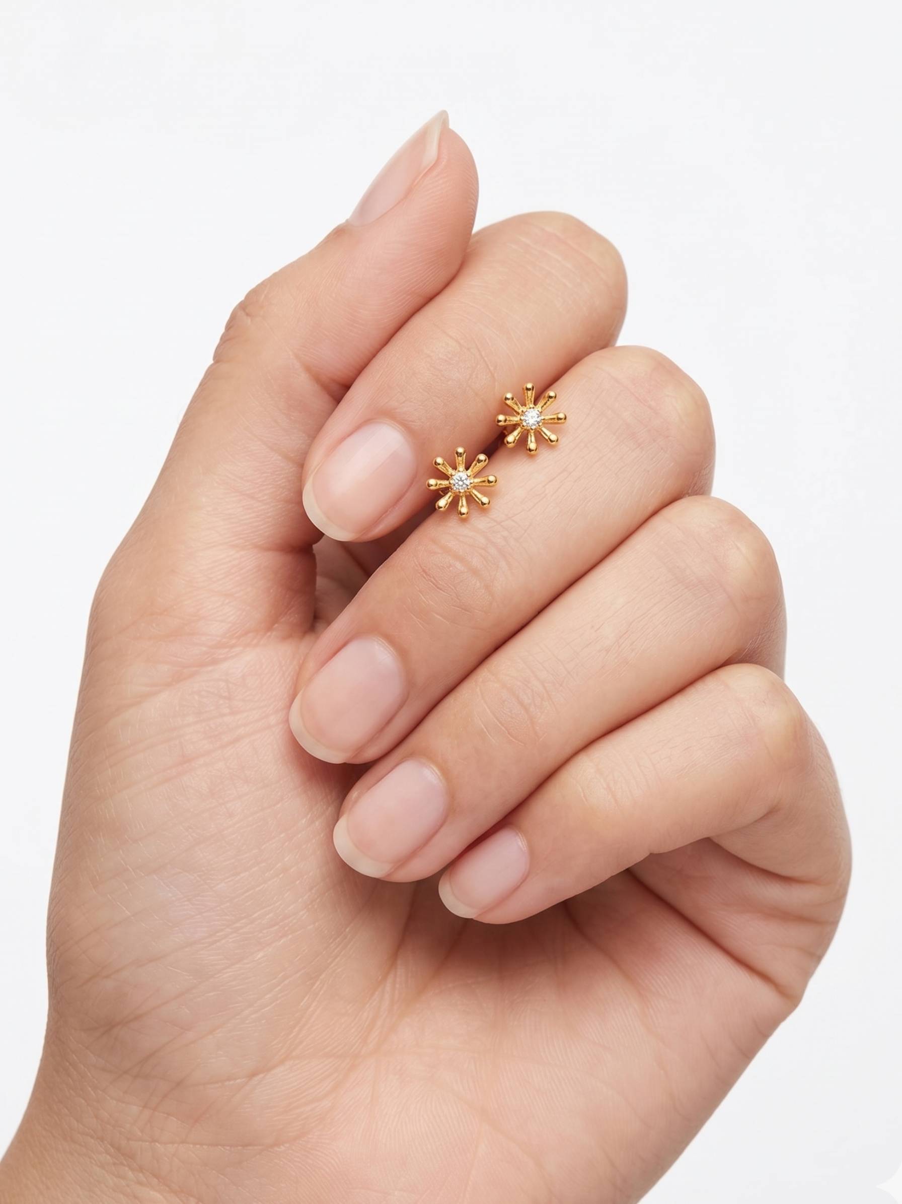 Gold star-shaped earrings held between fingers against a light background