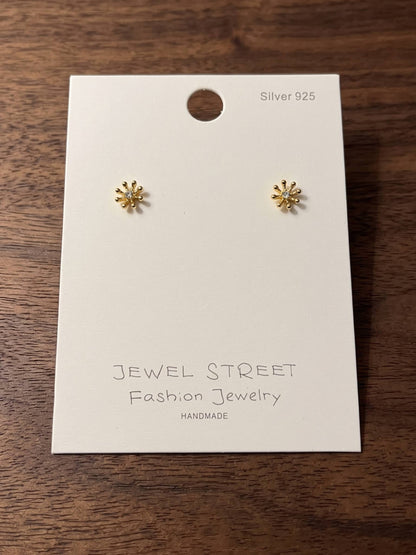 Gold flower-shaped earrings on a 'Jewel Street' branded card against a wooden background
