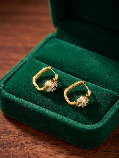 Gold earrings with gemstones on a green velvet cushion