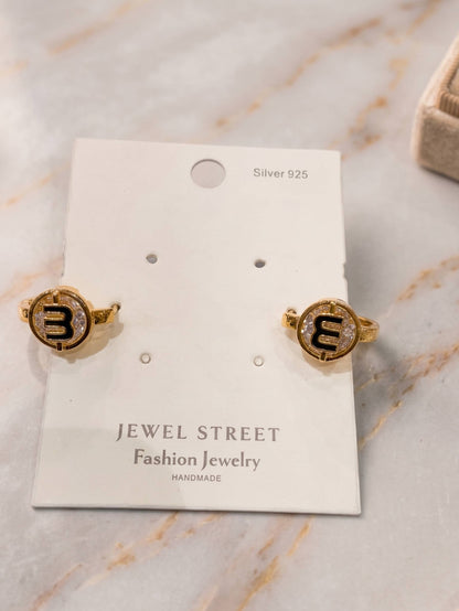 Gold earrings with letter 'M' on a Jewel Street card against a marble background