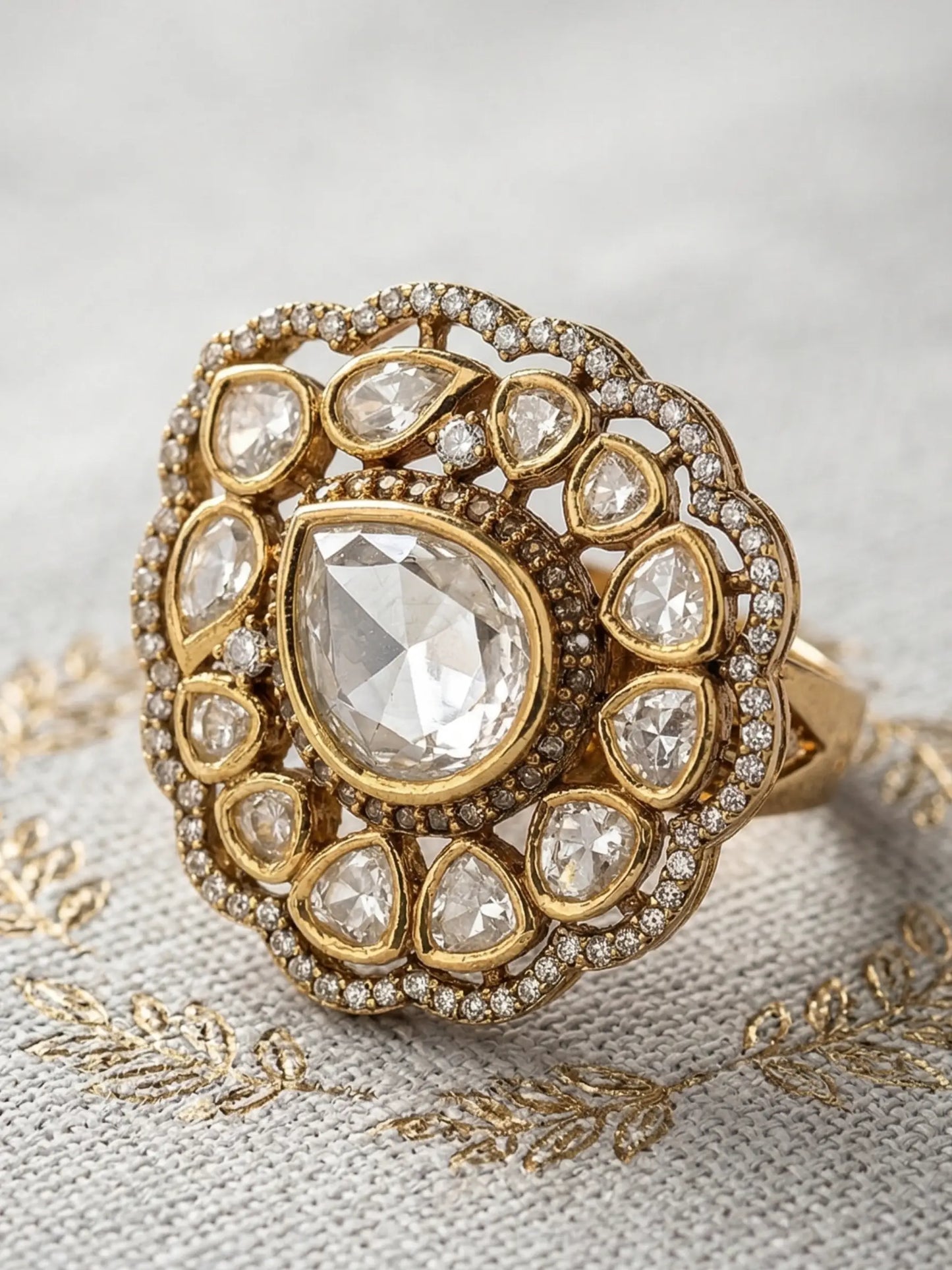 Gold ring with a large central diamond and smaller diamonds in a decorative setting on a textured fabric background.