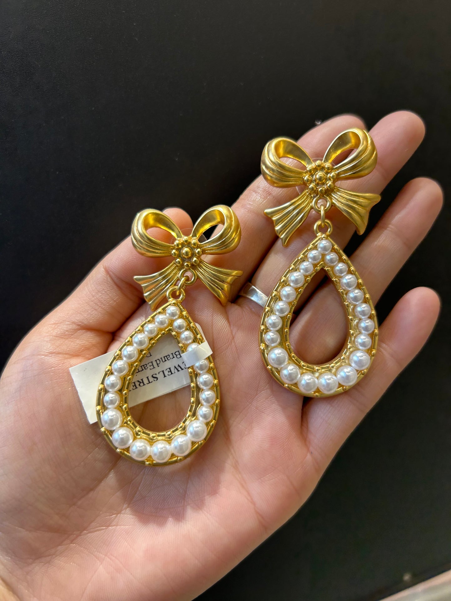 Close-up of a model wearing large gold-plated pearl earrings with a bow stud
