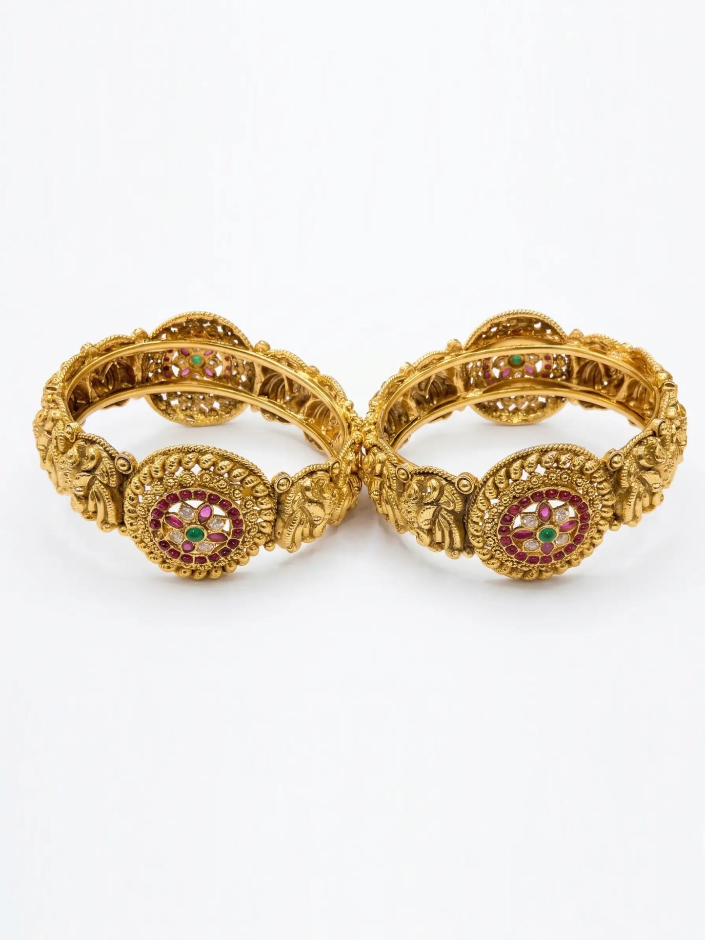 Pair of gold bangles with intricate designs and red gemstones on a white background