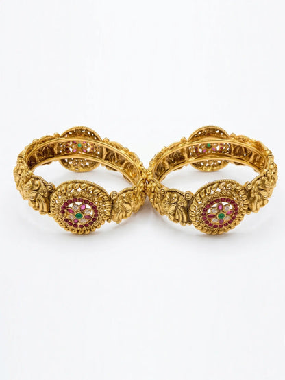 Pair of gold bangles with intricate designs and red gemstones on a white background