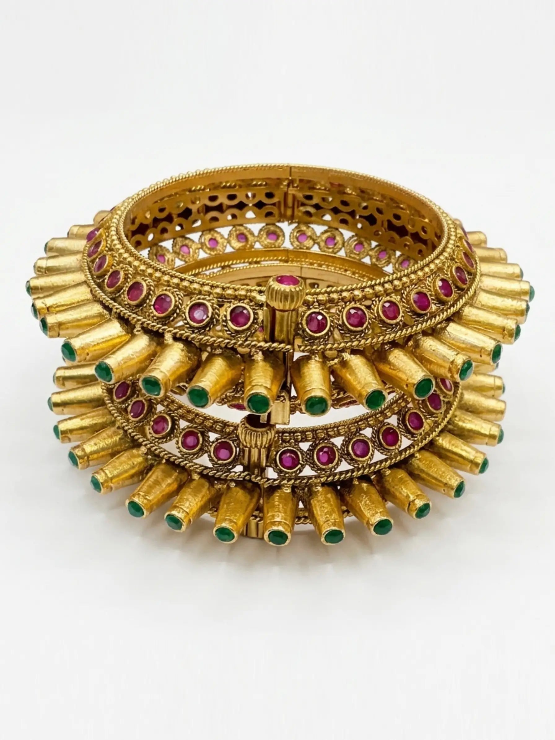 Gold bangles with red and green stones on a white background