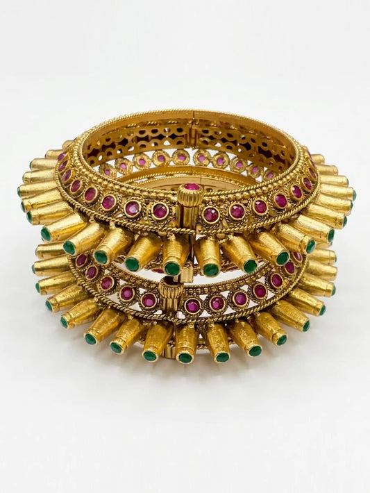 Gold bangles with red and green stones on a white background