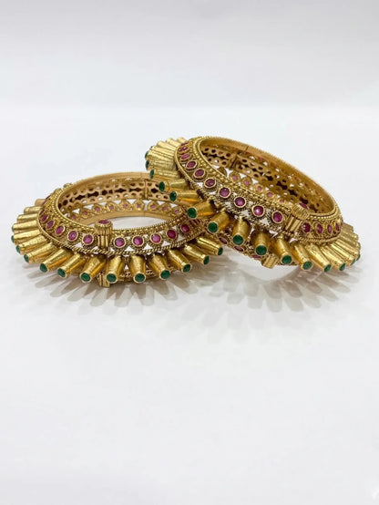 Pair of gold bangles with gemstones on a white background