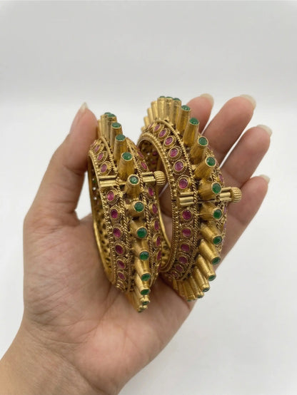 Gold bangles with gemstones held in a hand against a white background