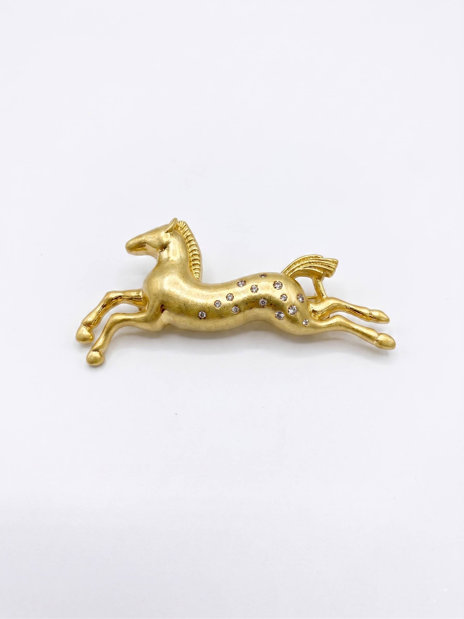 Gold horse-shaped brooch with embedded stones on a white background