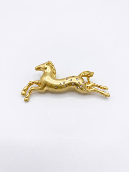 Gold horse-shaped brooch with embedded stones on a white background